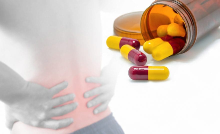 man grabbing lower back in pain and a bottle of pain medication open with capsules out of bottle